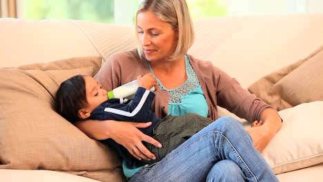 Junge-Mutter-Füttert-Ihr-Kleinkind-Mit-Der-Flasche-Auf-Einem-Sofa