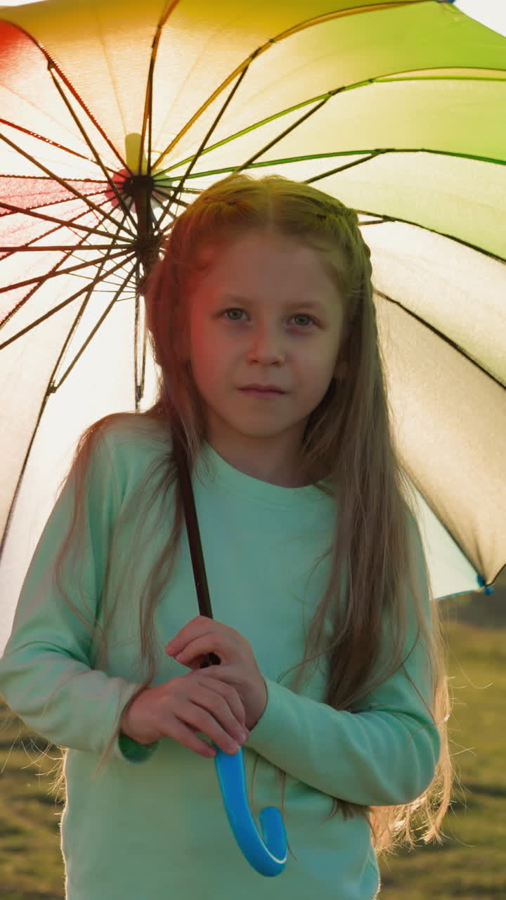 niño gira el paraguas en la orilla del río en la lluvia. niña bonita juega con un gran paraguas de colores en un día de verano lluvioso. niño encantador camina en el prado del país