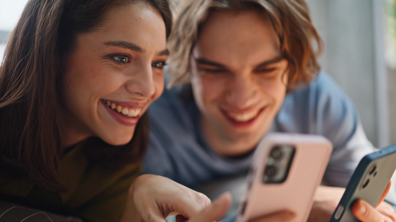 Hands holding two smartphones closeup. Laughing couple holding mobile devices