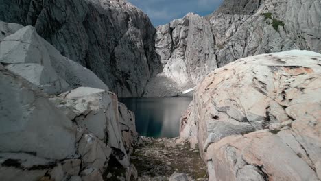 Drone-Pasando-A-Través-De-Un-Portal-De-Rocas-De-Granito-En-Dirección-A-Una-Laguna-Azul