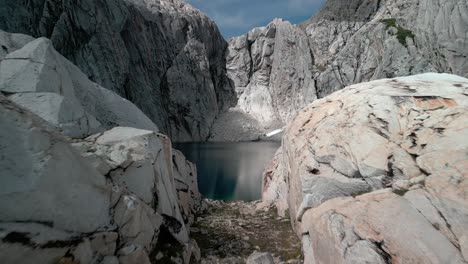drone pasando a través de un portal de rocas de granito en dirección a una laguna azul