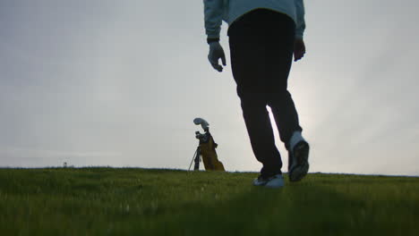 a golfer walking towards their golf bag on the field with the sun in the background