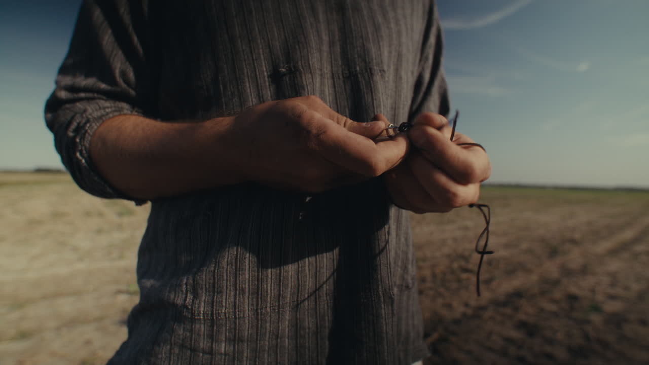 Close-up of hands threading an object onto a string in an outdoor field