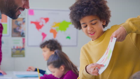 boy showing work to male teacher in classroom lesson