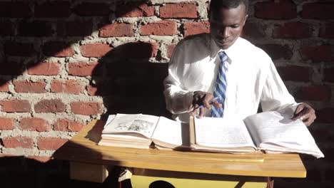 Eine-Zeitlupen-Schiebeaufnahme-Eines-Männlichen-Afrikanischen-Jugendlichen,-Der-Seine-Bücher-In-Einer-Heruntergekommenen-Schule-In-Einer-Armen-Gemeinde-Studiert