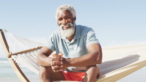 retrato de un anciano afroamericano feliz sentado en una hamaca en una playa soleada