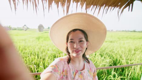 Bonita-Mujer-Asiática-Haciendo-Una-Videollamada-Que-Muestra-Un-Gran-Campo-De-Producción-De-Arroz