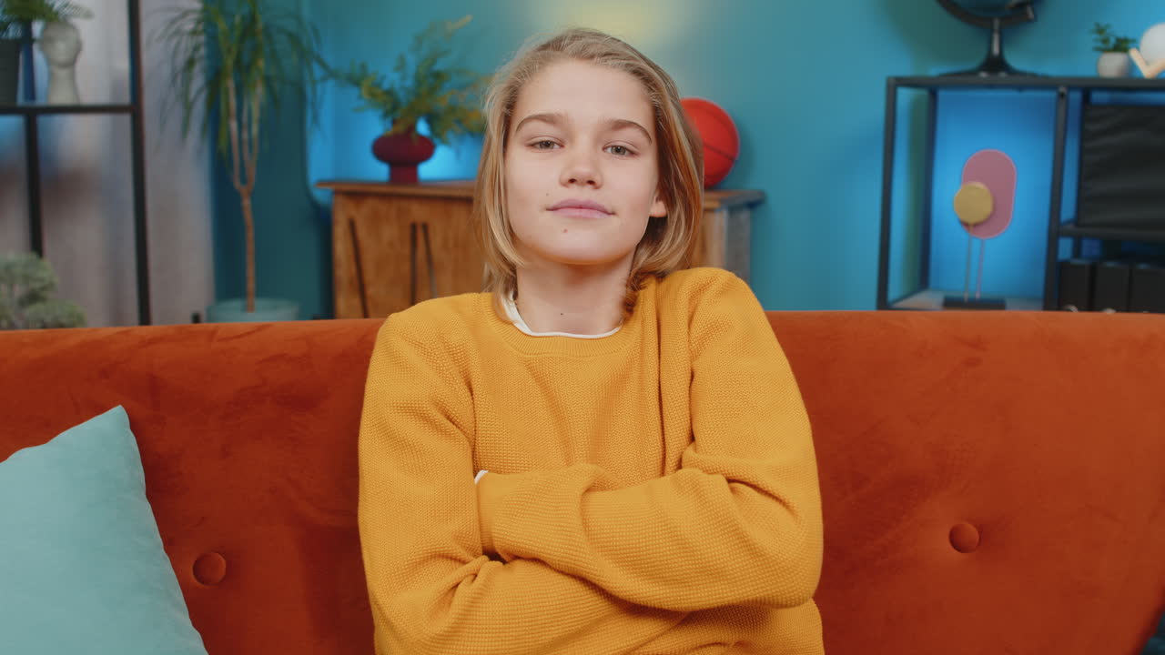 Teenager boy portrait with sincere smile sitting on sofa with folded arms looking at camera at home