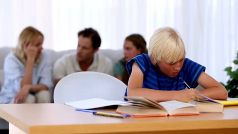 Son-doing-his-homework-with-family-on-couch-behind