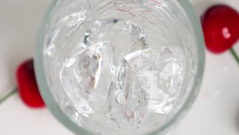 close up birdseye shot of clear ice cubes falling into a beautiful glass for a cool drink while cherries lie on the side in slow motion