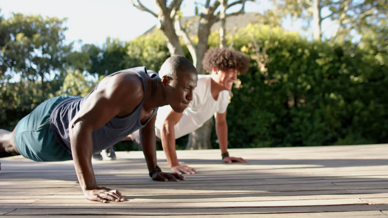 Exercising outdoors, two multiracial male friends doing push-ups on wooden deck, enjoying workout