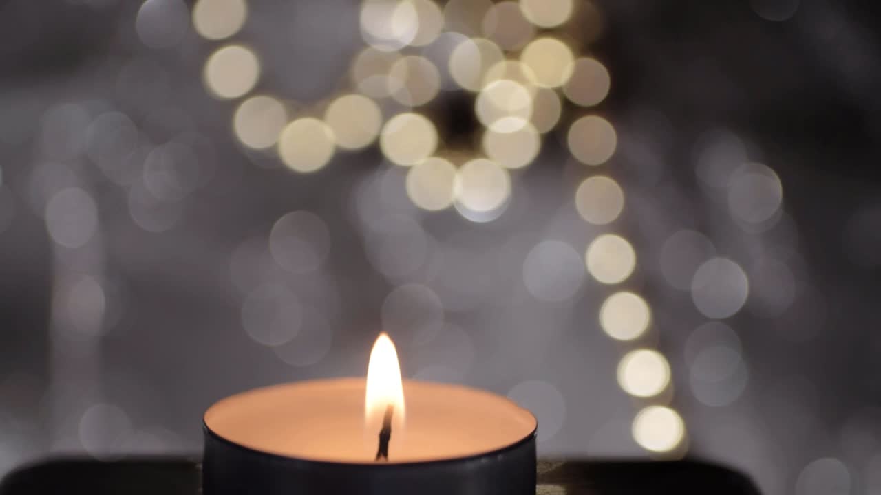 Detailní záběr jedné čajové svíčky se zlatým a stříbrným bokeh pozadím