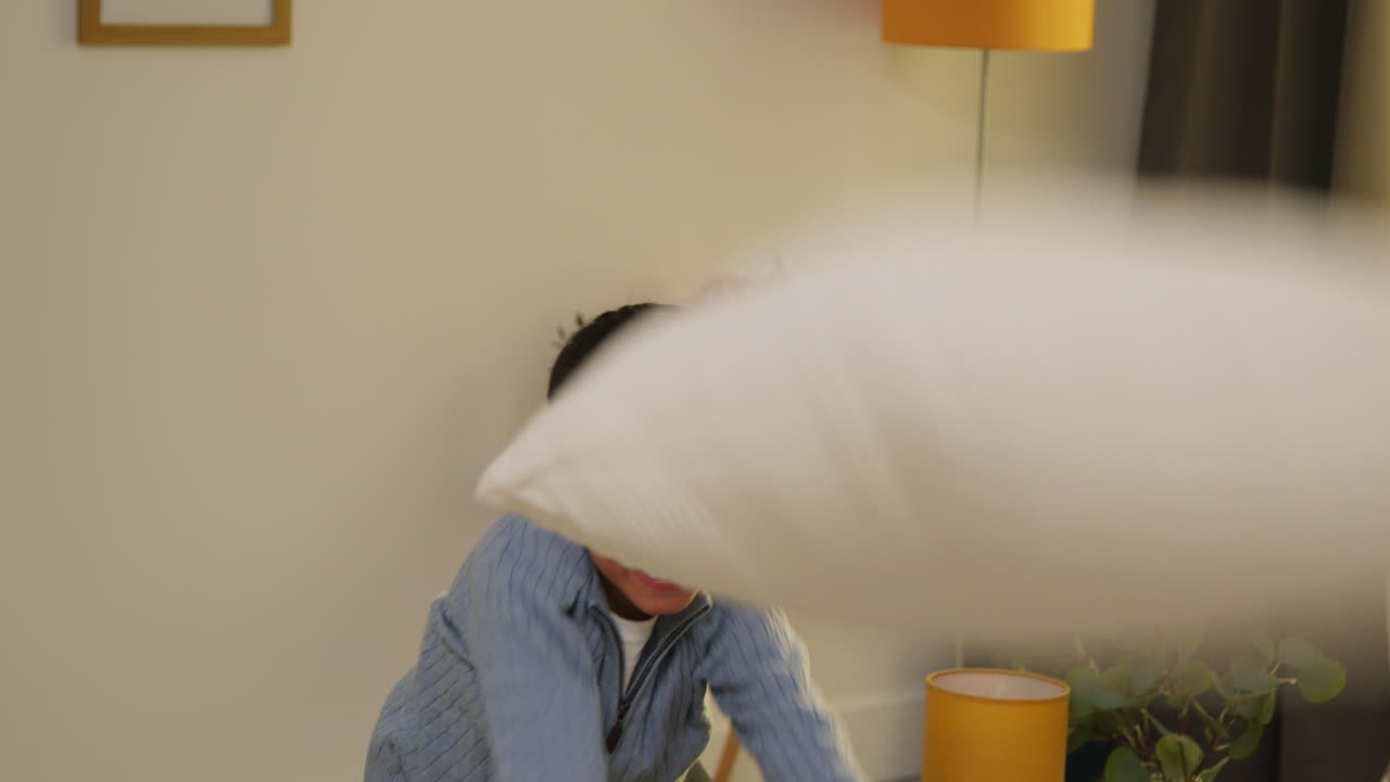 집에서 나게 행동하는 혼란스러운 어린 소년, 소파에 뛰어들고 라운지 1 주변에 베개를 던집니다.