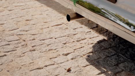 close up of an old classic car exhaust pipe over cobblestone pavement
