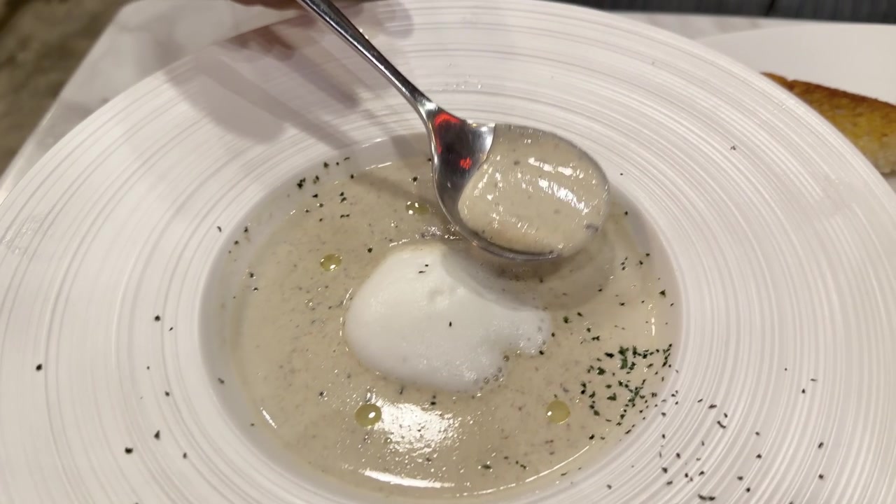 Servieren von cremiger Pilzsuppe mit einem Löffel und Knoblauchbrot