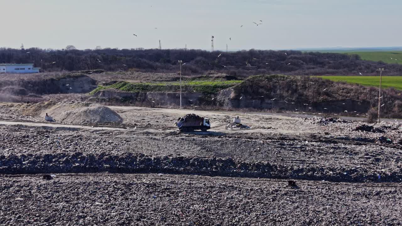 Camion industriale che si muove tra colline di rifiuti.