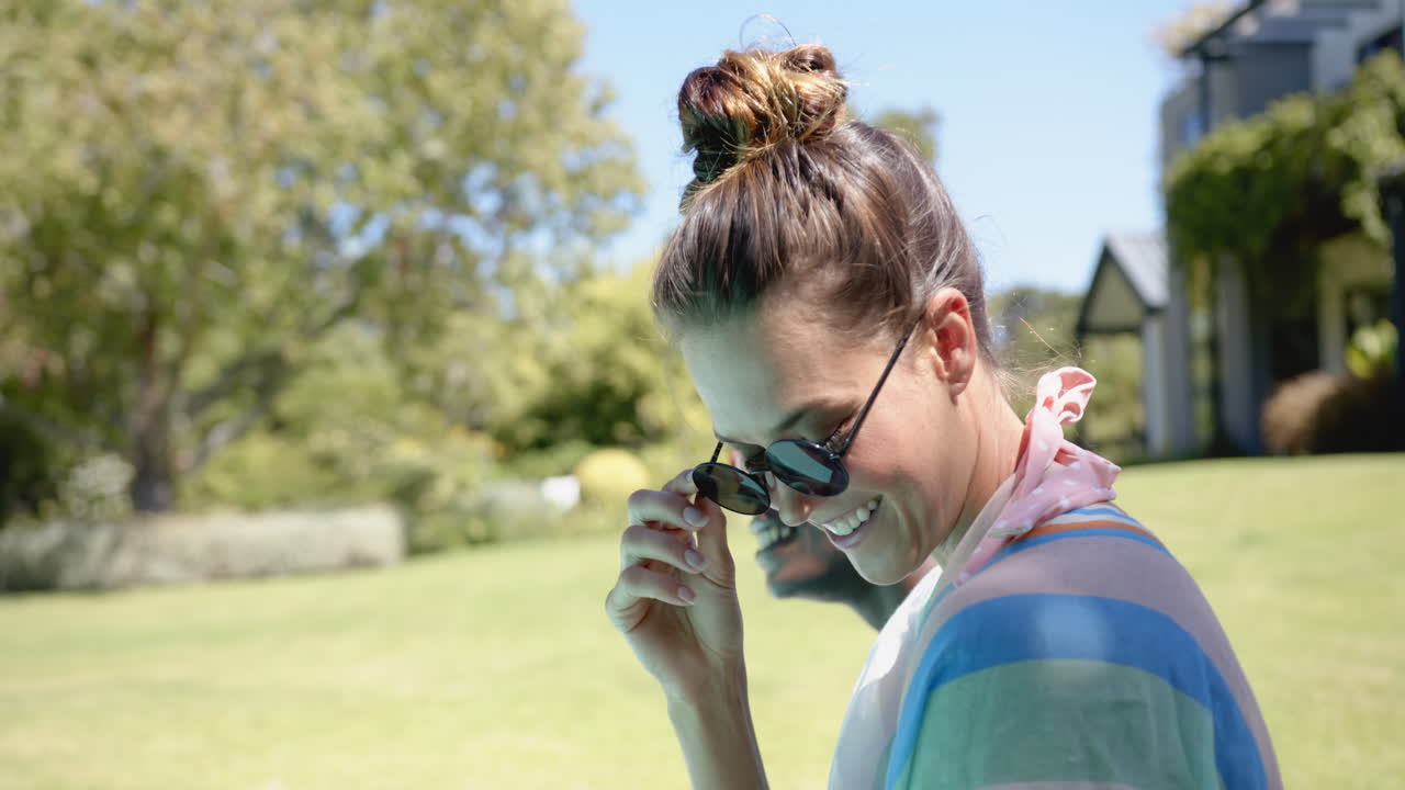Woman wearing sunglasses and smiling, enjoying sunny day outdoors in garden, copy space