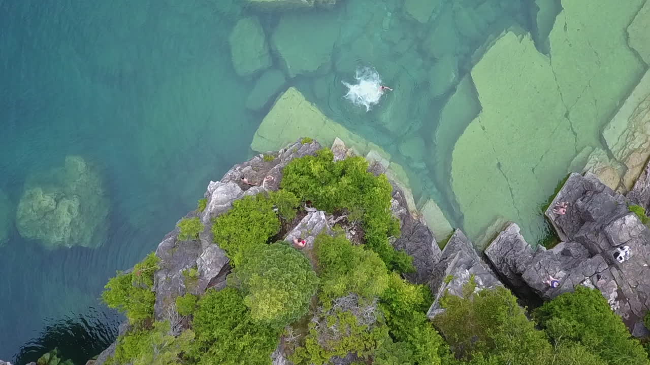 젊은 남자는 절벽에서 멀리 떨어진 맑은 녹색 호수 물 속으로 뛰어든다