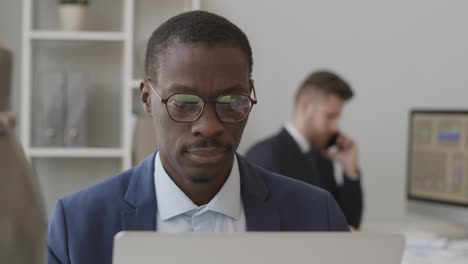 african american trader in eyeglasses working on laptop