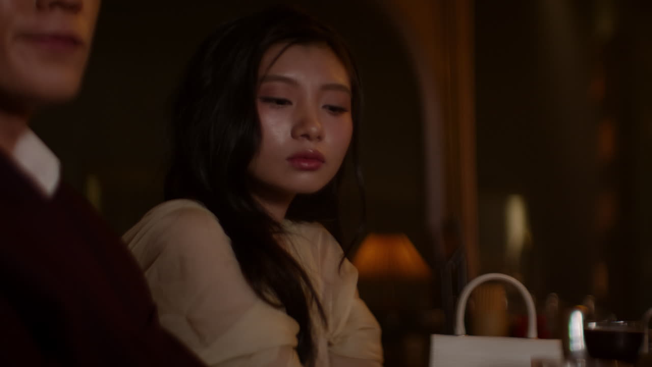 A young woman sits quietly at a bar, appearing upset, while the man beside her stays silent