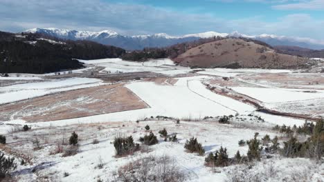 Vista-Aérea-Campos-Montañosos-Cubiertos-De-Nieve-Y-Picos-En-Un-Soleado-Día-De-Invierno