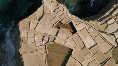 toma aérea de seguimiento de ángulo alto de un hombre caminando a través de charcos de salinas en xwejni durante una hermosa puesta de sol