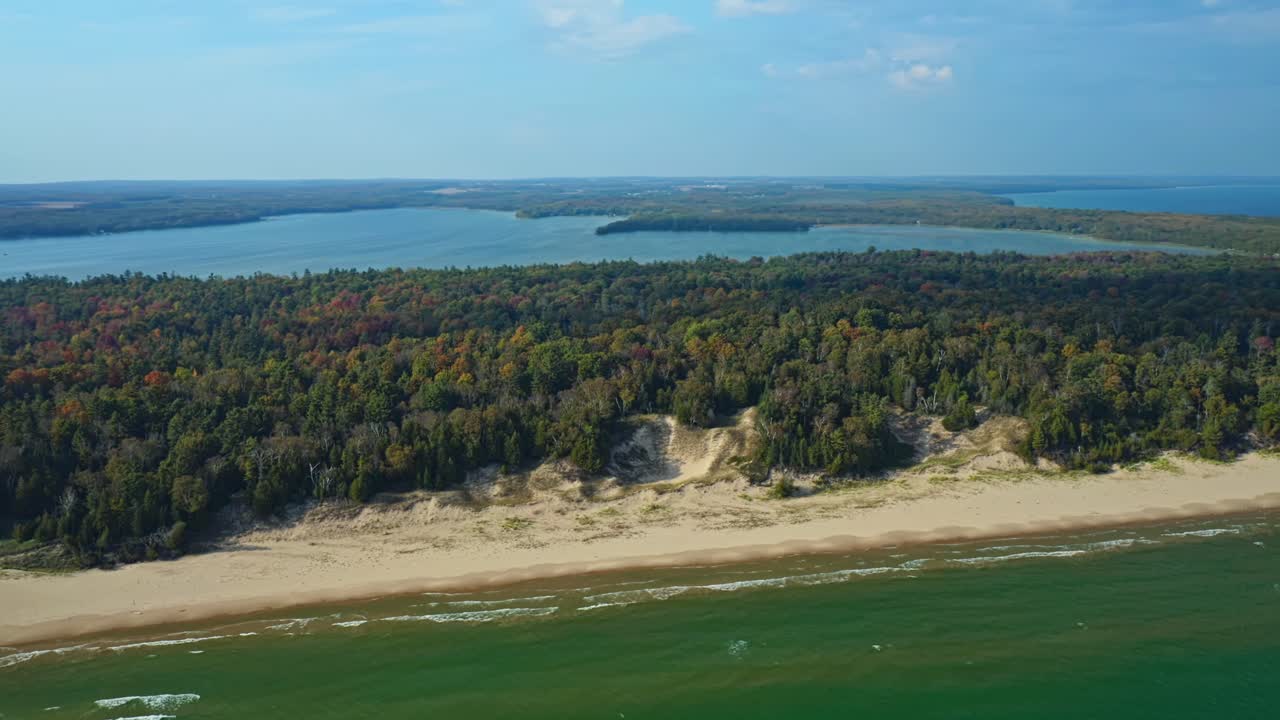Wind-shaped dunes rise behind a golden beach where green waves meet the edge of Door County’s forest, revealing the wild natural beauty of Lake Michigan’s eastern shore