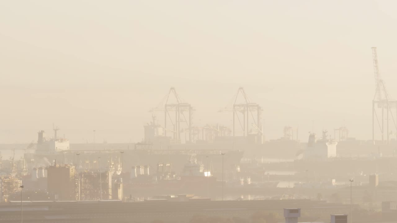 General view of cityscape with multiple buildings and shipyard covered in fog