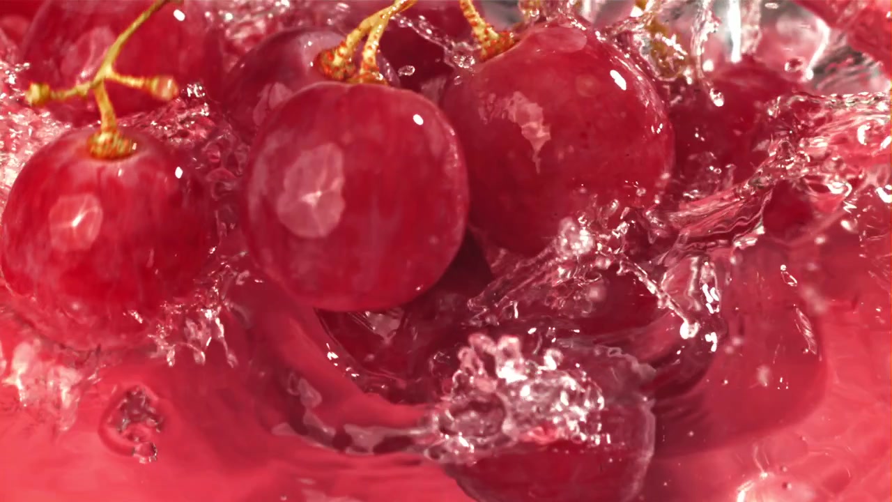 Uva rossa che cade nell'acqua con schizzi al rallentatore.