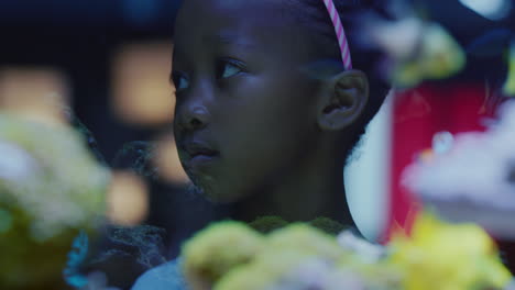 african-american-girl-looking-at-fish-in-aquarium-curious-child-watching-colorful-sea-life-swimming-in-tank-learning-about-marine-animals-in-underwater-ecosystem-inquisitive-kid-at-oceanarium