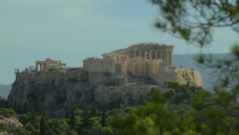 Close-up-of-the-Acropolis-with-tourists,-framed-by-foliage