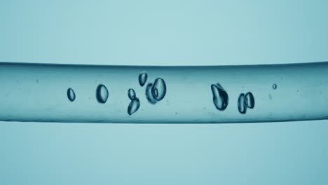 transparent glass tube with flowing clear water and air bubbles on a blue background transparent glass tube with flowing clear water and air bubbles on a blue background macro shot of the movement of a liquid substance with formation of bubbles concept of chemical or biological research in laborator