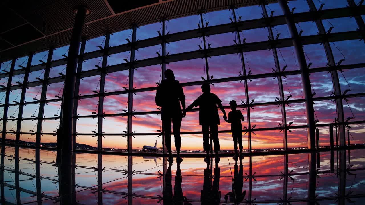 Silhouetted family at airport window during sunset, wide-angle shot