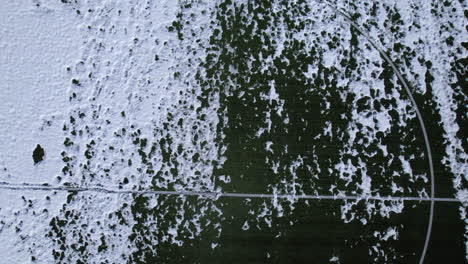 Ascending-birds-eye-view-of-the-famous-soccer-field-Heningsvær-Norway-partially-covered-in-snow,-with-footprints