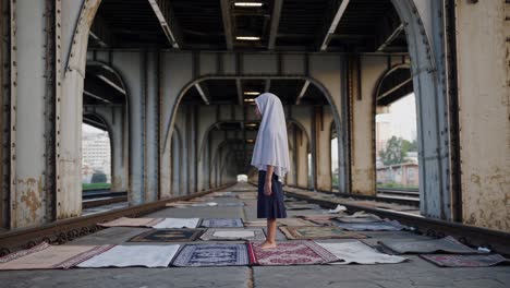 muslim girl standing on a prayer rug, praying under a bridge on a railway, creating a serene and spiritual atmosphere amidst an urban backdrop