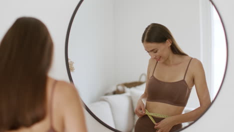 woman measuring waist in mirror