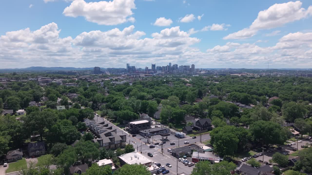 Lush green trees covering residential area with Nashville skyline in background under beautiful cloudy sky. Aerial, establishing push forward