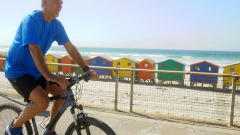 Side-view-of-active-senior-Caucasian-man-riding-bicycle-on-a-promenade-at-beach-4k