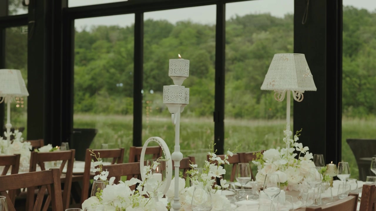 Elegant wedding reception venue featuring beautifully decorated banquet tables with white floral centerpieces, candles, wine glasses, and sophisticated table settings.