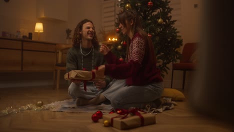 una pareja abriendo regalos de navidad junto al árbol.