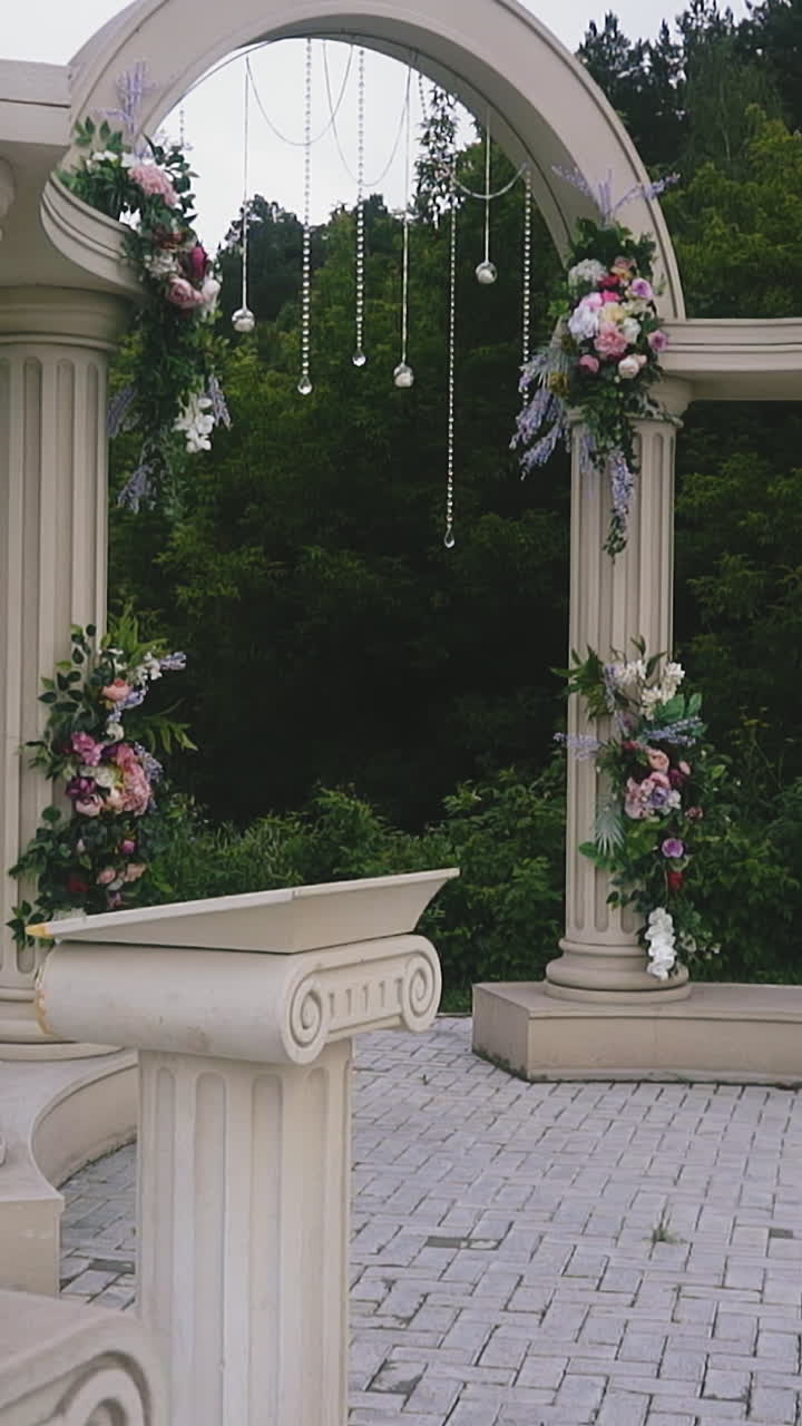 Slow motion: stylish vintage wedding venue with beautiful antique arch and columns decorated with plants near green trees on cloudy spring day