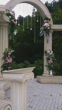 slow motion: stylish vintage wedding venue with beautiful antique arch and columns decorated with plants near green trees on cloudy spring day
