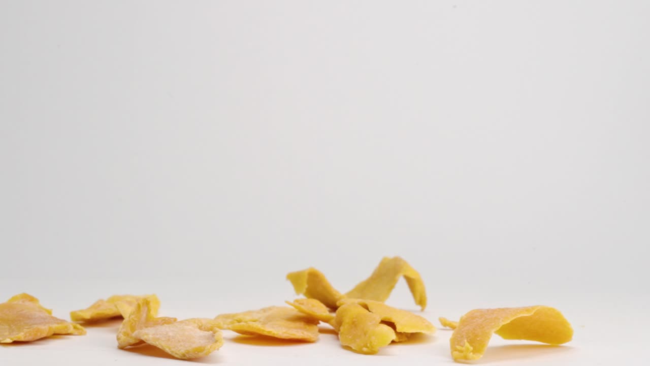 Dehydrated dried mango pieces falling onto white table top and bouncing and landing in a pile in slow motion