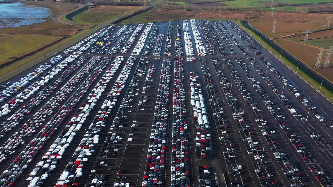 Drone shot of a industry lot, filled with new cars, flying forwards and panning up.