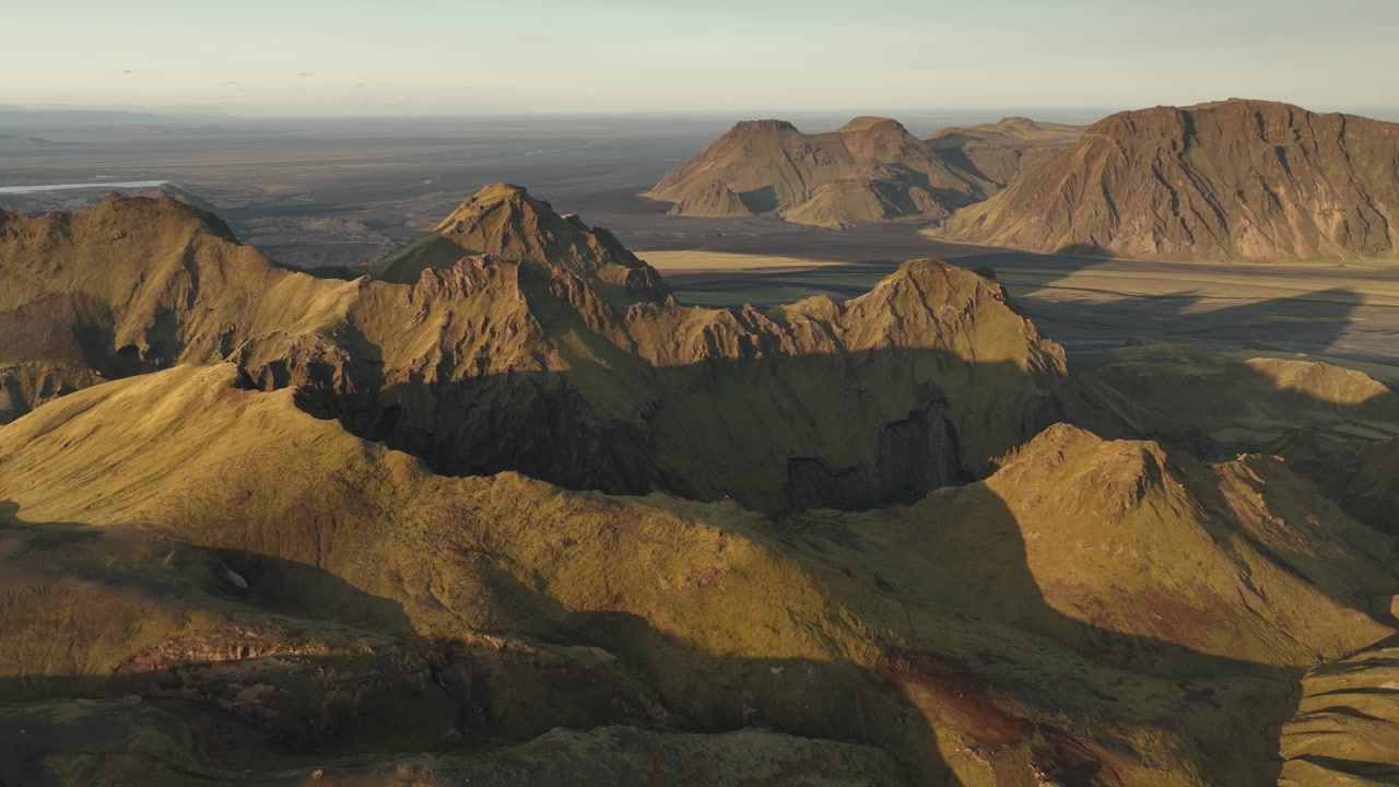 Una suggestiva vista aerea di Thakgil, Islanda, che mostra cime vulcaniche dai toni dorati che proiettano ombre profonde attraverso il vasto paesaggio aspro.