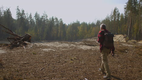 aged-fisherman-is-going-to-forest-lake-approaching-to-edge-of-cliff-on-high-shore-angling-and-hiking-at-sunny-fall-day