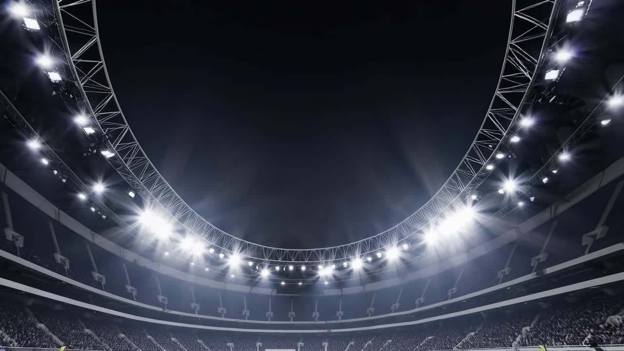 Empty soccer field illuminated by spotlights in a big stadium during night time, with blurred crowd in the stands and some staff members on the sideline