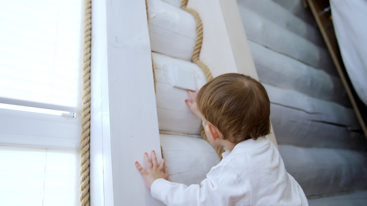 Cute toddler baby with a pacifier in mouth stands at the wall. Low angle view at the curious kid touching a light switch.