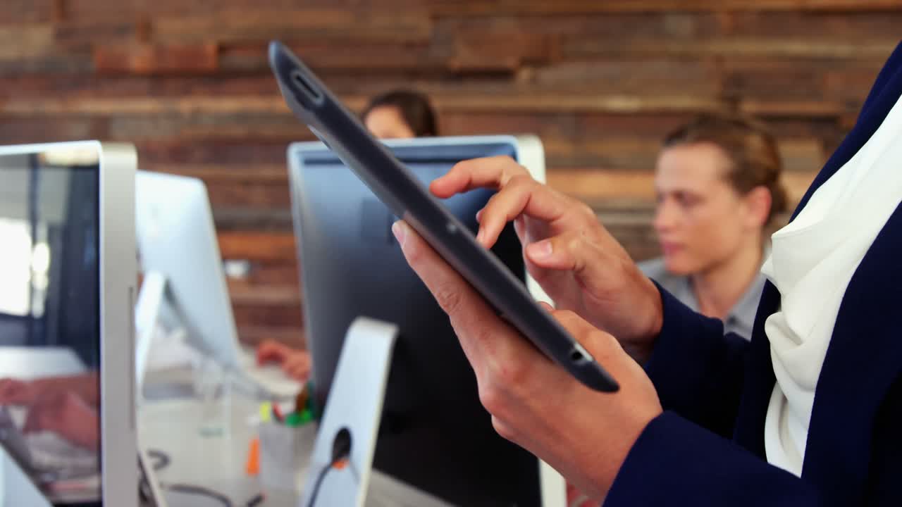 Female business executive using digital tablet while colleague working at desk