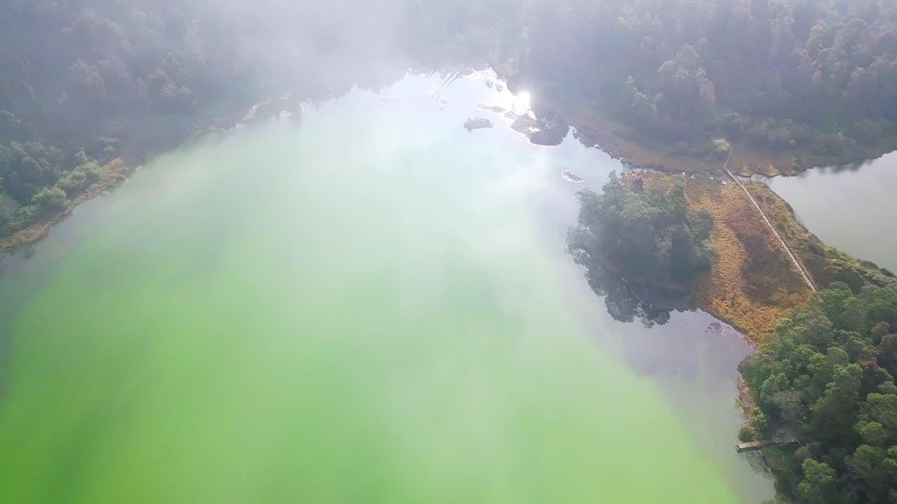 Aerial top down shot of exotic lake lighting by sun surrounded by deep forest scenery in Indonesia